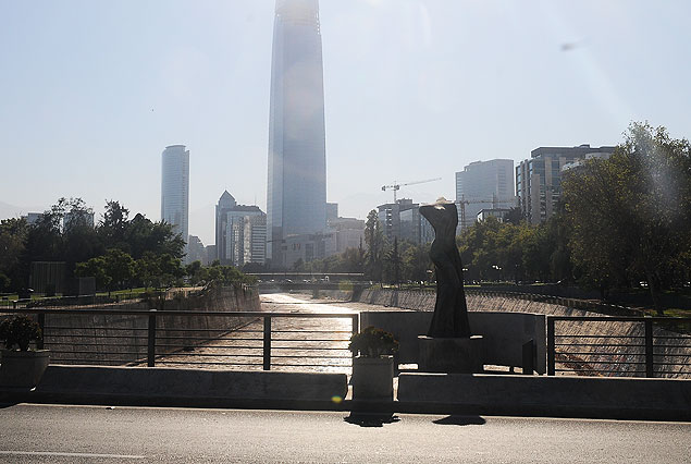 El curso del Mapocho parece de plata. Una escultura en primer plano y atrás una de los giganstecos edificios modernos de Santiago.