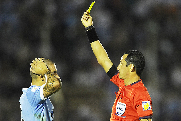 El árbitro paraguayo Arias le muestra la tarjeta amarilla a Maxi Pereira que se toma la cabeza.