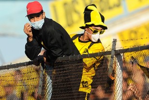 Dos ¿hinchas? de Peñarol con tapabocas trepados al alambrado perimetral de la Tribuna Brasil. 