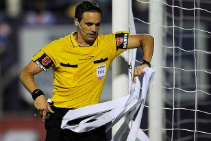 El árbitro argentino Patricio Loustau retira una serpentina de la cancha.
