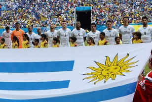 El equipo uruguayo vestido de blanco escuchando y cantando el himno de la patria.