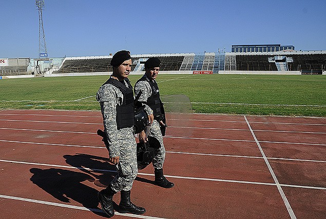 Los policías caminan por la pista de atletismo, al fondo tribunas vacías en el estadio Tróccoli. 